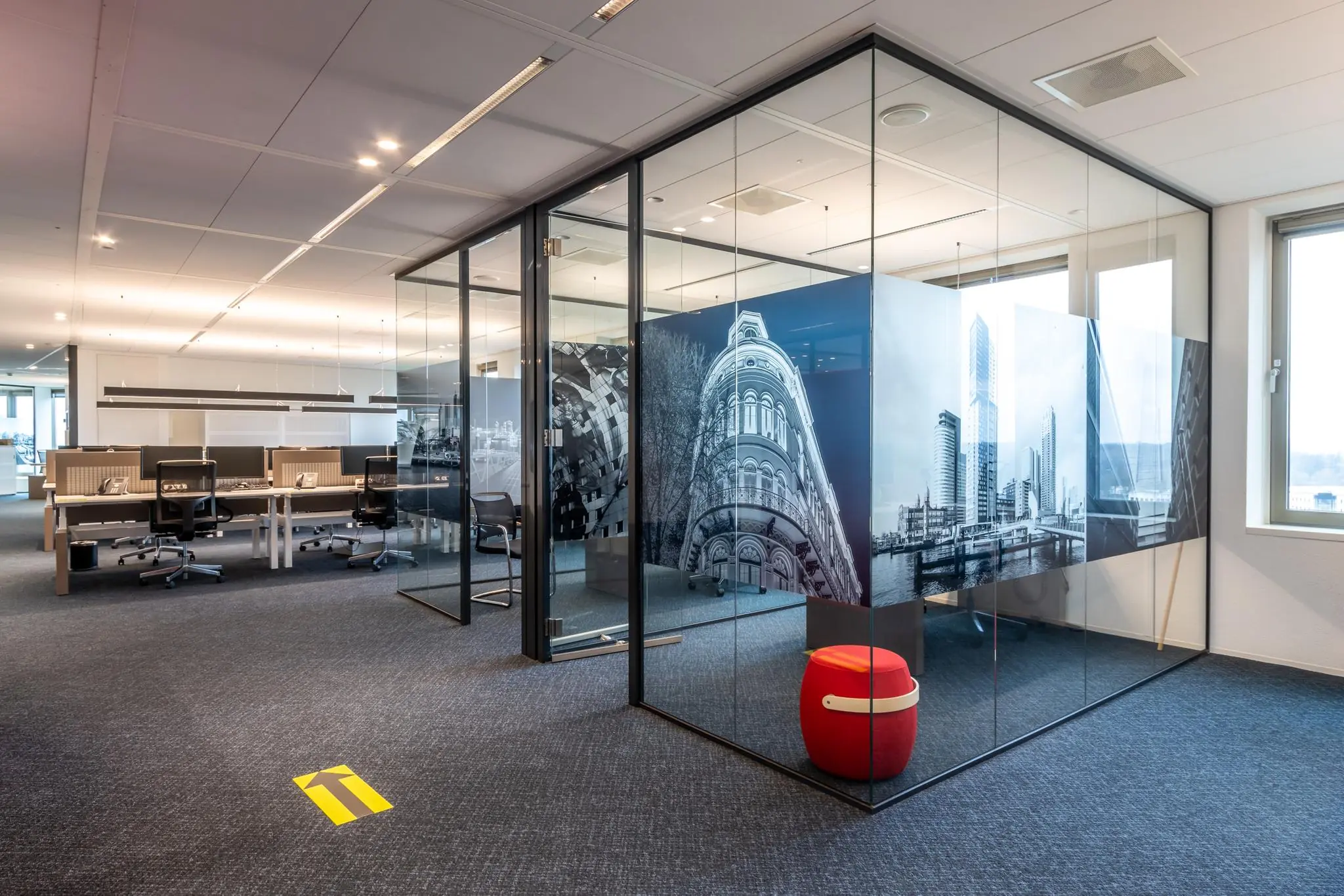 Modern kantoorinterieur met glazen vergaderruimte, fotowand van de Fascinatio Boulevard en werkplekken op de achtergrond.